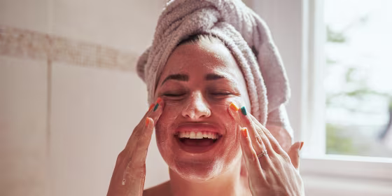 Woman smiling and scrubbing her face in the bathroom