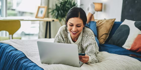 Shot of a young woman using a laptop and credit card on the bed at home