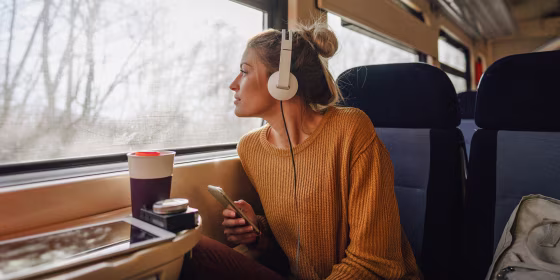 Photo of a young woman riding on a train, enjoying her trip while looking through the window and listening to some music on her mobile phone