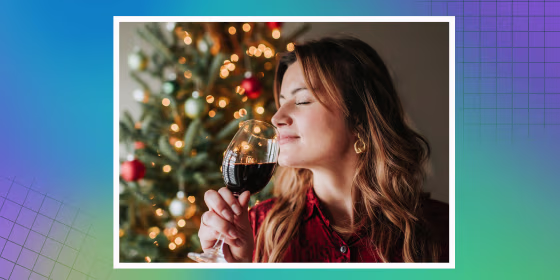 Woman smelling glass of wine beside decorated Christmas tree