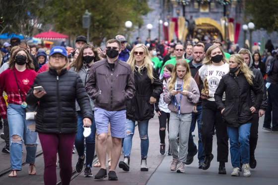 Visitors, some wearing face masks, others not, walk down Main Street USA at Disneyland in Anaheim, Calif., on Dec. 27, 2021.
