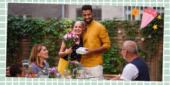 Happy young man with bouquet and gift hugging his senior mother in law outdoors in garden