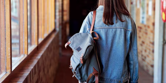 Rear view of young woman with backpack walking in corridor at university