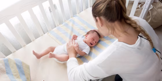 Mother sitting near the cradle and holding baby's hand