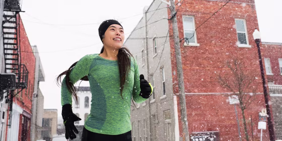 Happy young female runner in knit hat running in snowy stree