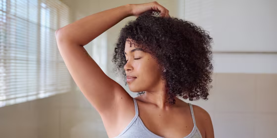 Shot of a beautiful young woman smelling her underarms at home