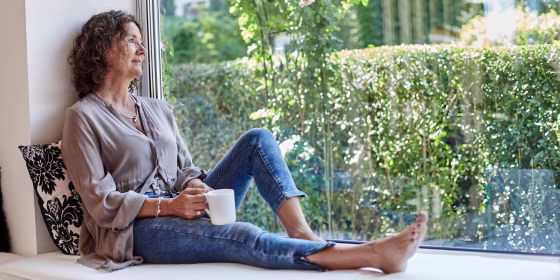 Mature woman sitting at the window at home with cup of coffe