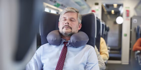 Tired businessman with neck pillow sleeping on passenger train