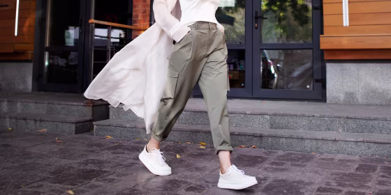 street fashion style. Beautiful Sexy Woman Wearing Fashionable Spring Or Fall Clothes (beige trench coat, cargo pants, accessorie) Outdoors. Female stylish Model walking Street. Autumn trend