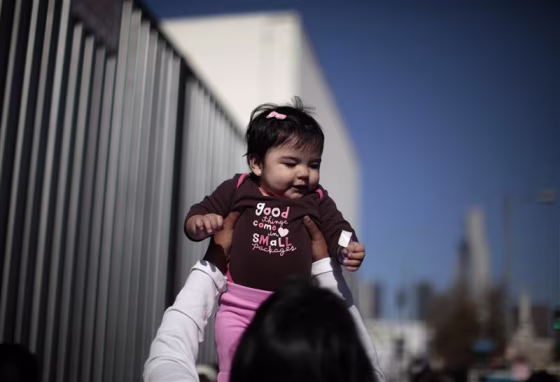 A woman plays with a baby as they wait to go into a \"Back-to-School\" giveaway at the Fred Jordan Mission in Los Angeles