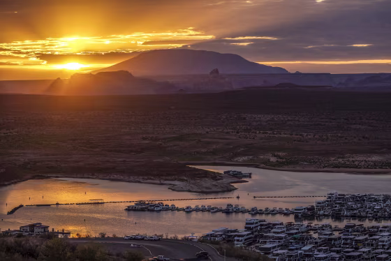 The sun rises behind Navajo Mountain and boats in Wahweap Bay at Lake Powell on Sept. 1, 2022 near Page, Ariz.
