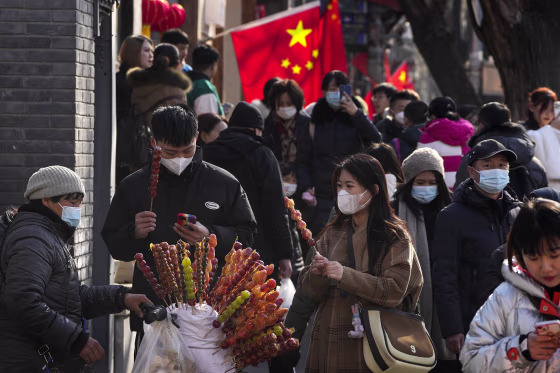 People buy sugar-coated Chinese haws as visitors tour a shopping street near the Drum Tower in Beijing, Monday, Jan. 30, 2023. Chinese people are enjoying the Lunar New Year and visiting various tourist sites in cities around China following the lifting last month of draconian COVID-19 restrictions, allowing a return to many aspects of normal life. (AP Photo/Andy Wong)