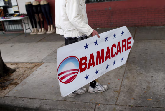 Image: Pedro Rojas holds a sign directing people to an insurance company where they can sign up for the Affordable Care Act, also known as Obamacare