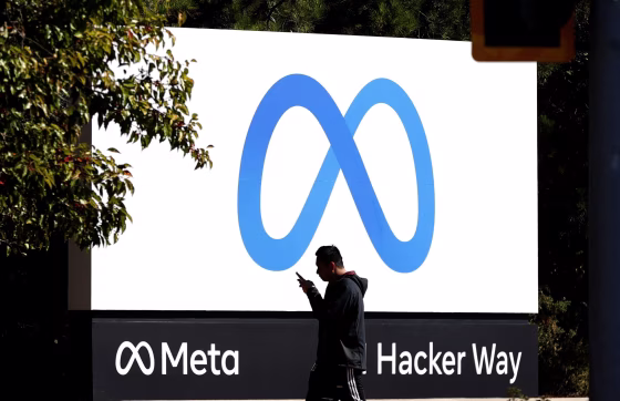 A pedestrian walks past a Meta sign in front of the company's headquarters