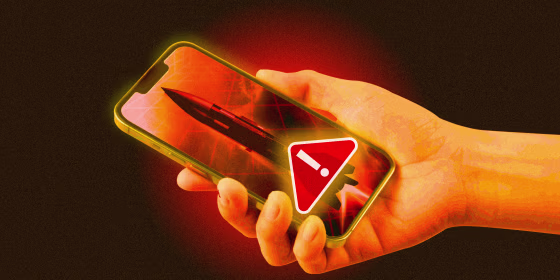 Hand holding phone; screen depicts rocket and red "warning" icon