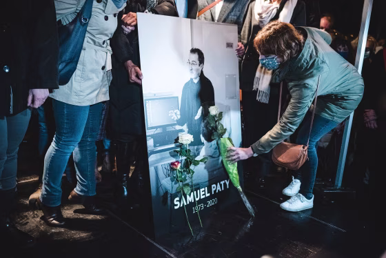 Relatives and colleagues gather around a portrait of Samuel Paty.