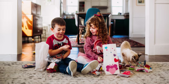 Two children sitting on the floor opening Valentines Day cards and gifts.