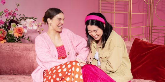 two women laughing while sitting on a sofa