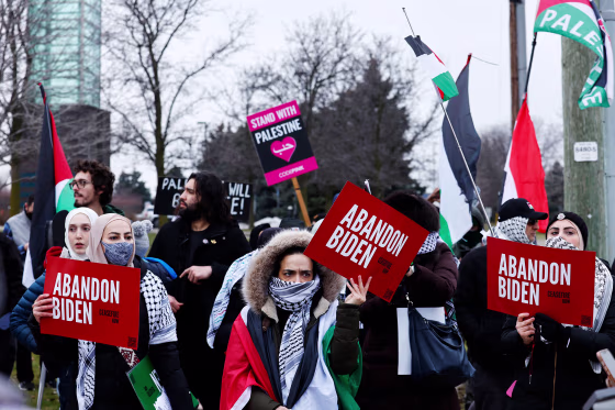 Pro-Palestinian protesters carry signs read, "Abandon Joe Biden" and "Stand with Palestine."