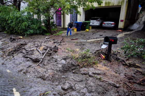A resident tries to sweep mud and debris from the driveway of his home