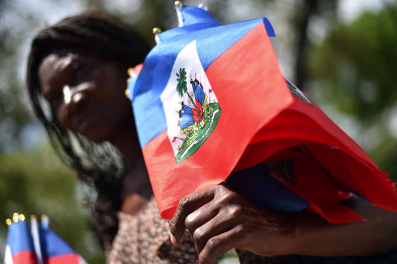 A woman sells Haitian national flags while looking at a group perform a dance during the celebration of Flag Day