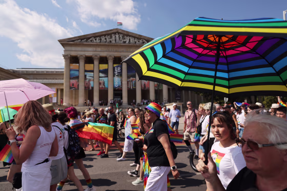 Attendees with umbrellas and rainbow flags march during Pride event. 