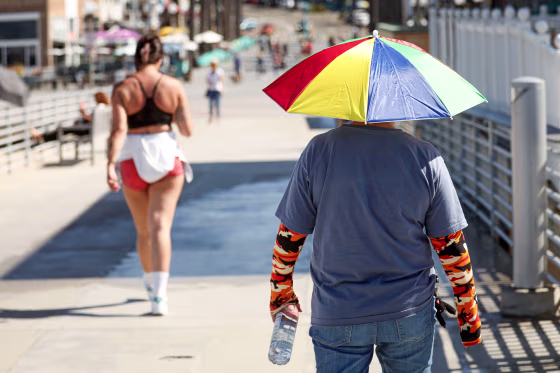 A person with an umbrella hat walks in the sun.