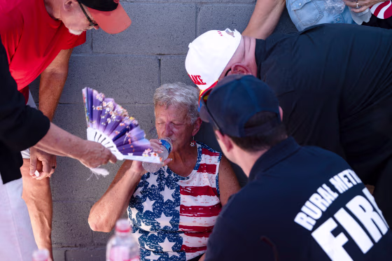 A woman drinks a bottle of water surrounded by people trying to help her