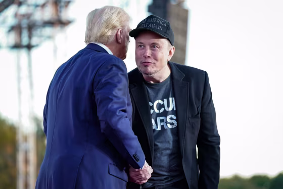 Elon Musk and Donald Trump shake hands on stage outside