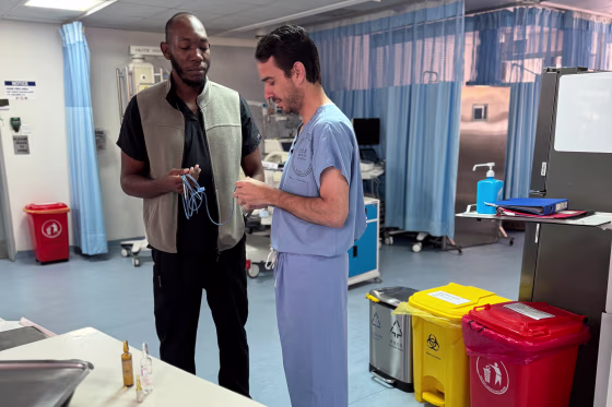 Cornel Sendagire, left, and Michael Lipnick stand in a hospital room and look at an item in Lipnick's hand