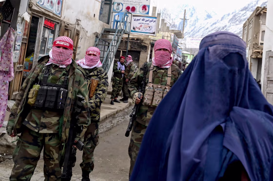 Taliban fighters stand guard as a burqa-clad woman walks along a street