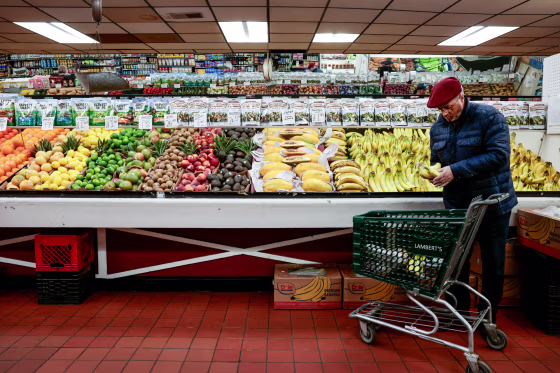 A person holds bananas near their shopping cart in the produce section of a grocery store