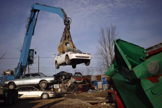 A crane loads a discarded automobile into a baler at a scrap yard
