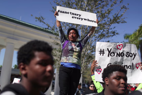 A woman holds a sign that says "#sanctuary everywhere"