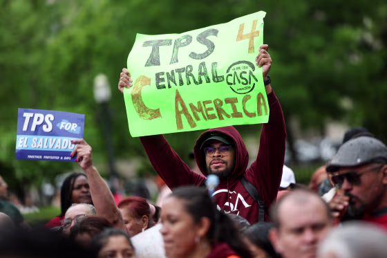 A person holds a green sign that reads "TPS 4 Central America"