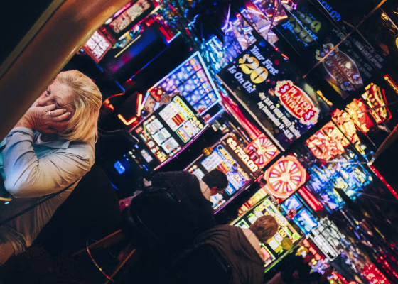 A woman holds her hand in her face while sitting at a slots machine.
