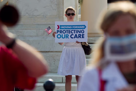 A demonstrator holds a sign that reads, "Moving Forward, Protecting Our Care"
