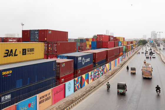 Vehicles move past a warehouse yard with shipping containers near port area in Karachi