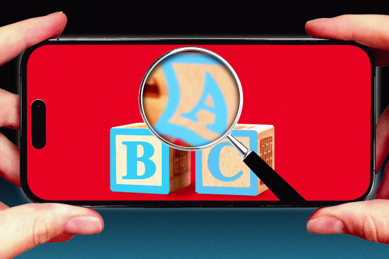 Photo illustration of hands holding phone, on the phone screen: a magnifying glass and ABC block letters 