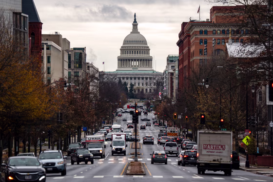 Vehicles crowd a six-lane street with the U.S. Capitol building visible in the background.