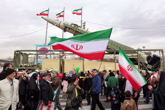People walk with Iranian national flags near a ballistic missile launch vehicle
