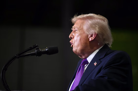 Donald Trump faces to the left while speaking into a microphone.