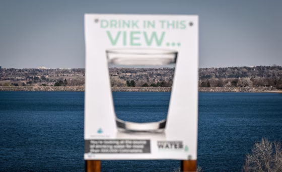 A sign with a water glass on it appears in soft focus in front of a large mountain lake.