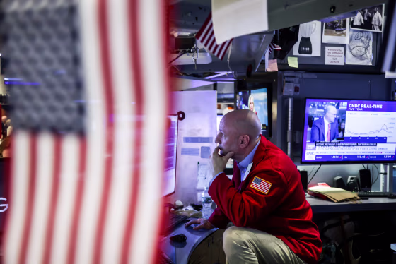 A person sits at a work desk with various monitors, an American flag covers half of the photo in the foreground