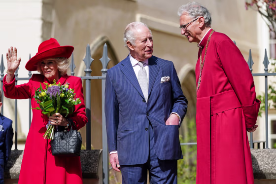 From left, Queen Camilla waves as King Charles, center, and Christopher Cocksworth speak outside
