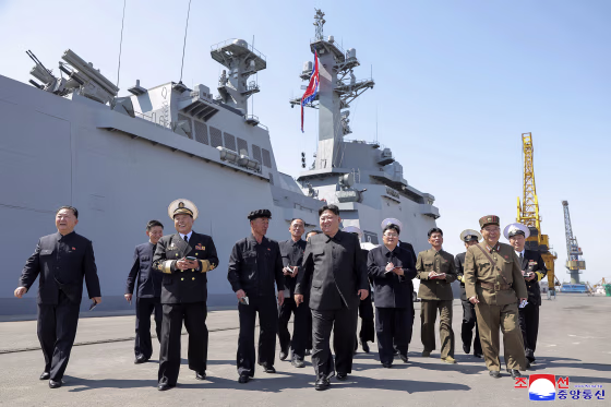 Kim Jong Un walking on a cement platform surrounded by other men in uniform.