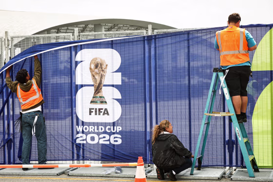 Workers affix FIFA World Cup 2026 logos and signage on a fence outside of SoFi Stadium