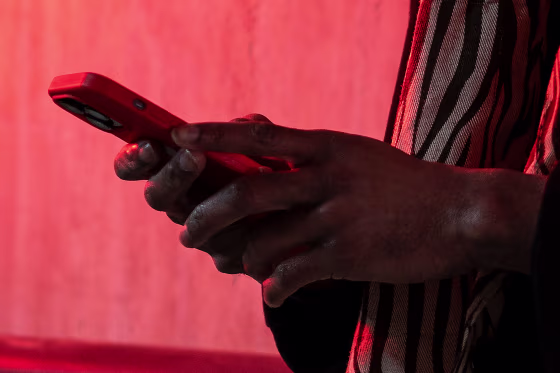 Image: A man holds a smartphone while standing near a wall with red neon lighting