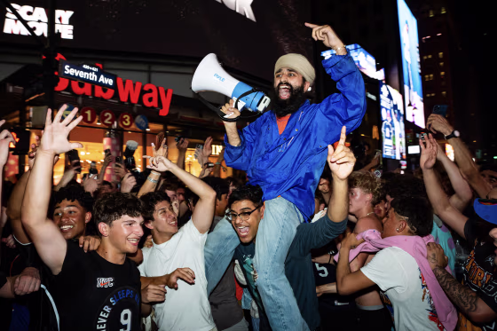 A man with a megaphone riding on someone's shoulders and surrounded by hundreds of other revelers.