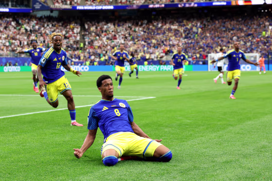 Livano Comenencia slides on his knees on the ground of the soccer field in celebration as his teammates run behind him